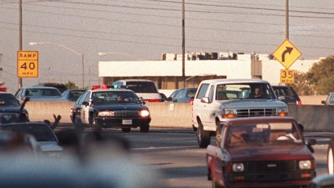 LOS ANGELES - JUNE 17: Motorists wave as police cars pursue the Ford Bronco (white, R) driven by Al Cowlings, carrying fugitive murder suspect O.J. Simpson, on a 90-minute slow-speed car chase June 17, 1994 on the 405 freeway in Los Angeles, California. Simpson's friend Cowlings eventually drove Simpson home, with Simpson ducked under the back passenger seat, to Brentwood where he surrendered after a stand-off with police. (Photo credit should read MIKE NELSON/AFP via Getty Images)