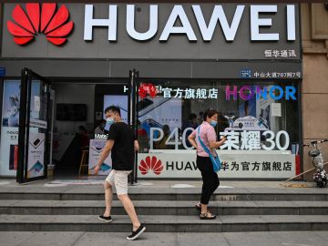People wearing face masks walk outside a Huawei store in Wuhan, in Chinas central Hubei province on May 26, 2020. (Photo by Hector RETAMAL / AFP) (Photo by HECTOR RETAMAL/AFP via Getty Images)