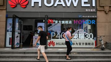 People wearing face masks walk outside a Huawei store in Wuhan, in Chinas central Hubei province on May 26, 2020. (Photo by Hector RETAMAL / AFP) (Photo by HECTOR RETAMAL/AFP via Getty Images)