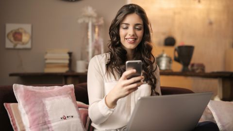 woman-sitting-on-sofa-while-looking-at-phone-with-laptop-on-920382