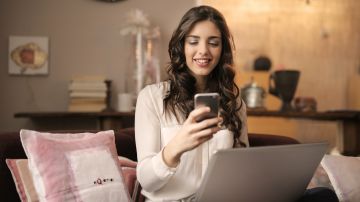 woman-sitting-on-sofa-while-looking-at-phone-with-laptop-on-920382