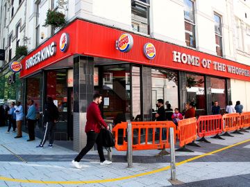 Shoppers maintain the British government's current social distancing guidelines and stand two metres (2M) apart as they queue to enter a Burger King fast Food store (R) and Next Store (L) in Cardiff on June 22, 2020, as some non-essential retailers in Wales are able to reopen from their enforced coronavirus shutdown. - Various stores and outdoor attractions in Wales are set to open Monday for the first time in nearly three months, as the government continues to ease its coronavirus lockdown, but pubs and restaurants must remain closed, and people must still stay 'local', where possible. (Photo by GEOFF CADDICK / AFP) (Photo by GEOFF CADDICK/AFP via Getty Images)
