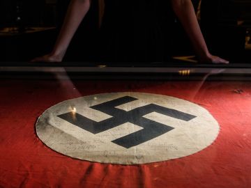 LONDON, ENGLAND - MARCH 15:  A gallery assistant poses with a captured Nazi swastika flag, signed by original members of the SAS, listing their missions in Africa during World War II, at the National Army Museum on March 15, 2018 in London, England. "Special Forces: In the Shadows" is a new exhibition, exploring the background and equipment used by the British Army Special Forces, and runs from 17 March to 18 November 2018.  (Photo by Leon Neal/Getty Images)