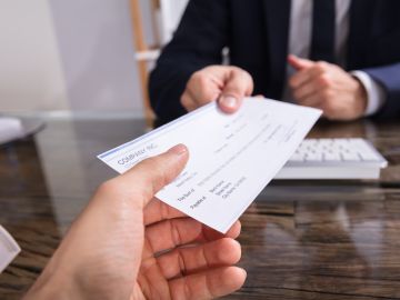 Foto de la mano de una persona recibiendo un cheque