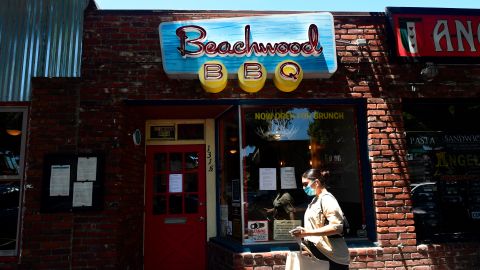 A pedestrian wearing a facemask walks past Beachwood BBQ restaurant, open for 14 years in Seal Beach, California on July 28, 2020, but closing soon due to the economic situation around the coronavirus pandemic. - This weekend, Beachwood BBQ, which had become a staple in the community, permanently shut down -- yet another casualty of the carnage the coronavirus pandemic has unleashed on restaurants across the United States. (Photo by Frederic J. BROWN / AFP) (Photo by FREDERIC J. BROWN/AFP via Getty Images)