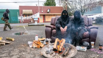 PORTLAND, OR - DECEMBER 10: Two protesters in black sit near a fire inside an eviction blockade on December 10, 2020 in Portland, Oregon. Police and protesters clashed during an attempted eviction Tuesday morning, leading protesters to establish a barricade around the Red House. (Photo by Nathan Howard/Getty Images)