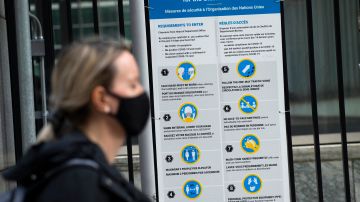 A woman wearing a facemask walks past a sign displaying Covid-19 safety requirements outside the United Nations in New York on March 11, 2021. - The virus has now killed more than 2.6 million people, subjected billions to anti-Covid restrictions, and left the global economy in tatters -- an outcome unimaginable at the outset of the crisis. (Photo by Kena Betancur / AFP) (Photo by KENA BETANCUR/AFP via Getty Images)