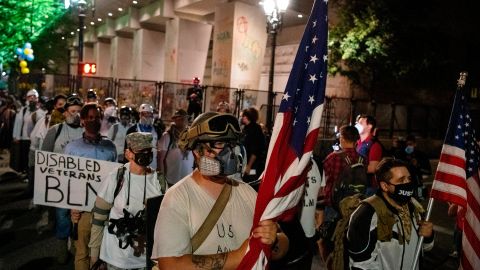 Members of the Wall of Vets, a group of military veterans, stand between the Mark O. Hatfield United States Courthouse and the Justice Center during a night of protest against racial injustice on July 31, 2020 in Portland, Oregon. - US federal officers will stay in the protest-wracked city of Portland until local law enforcement officials finish a "cleanup of anarchists and agitators," the US President said. The forces -- whose deployment was seen by many as part of the president's law-and-order strategy for re-election and exacerbated tensions between authorities and anti-racism protestors -- had been scheduled to begin their phased pullout from Portland on July 30. (Photo by Alisha JUCEVIC / AFP) (Photo by ALISHA JUCEVIC/AFP via Getty Images)