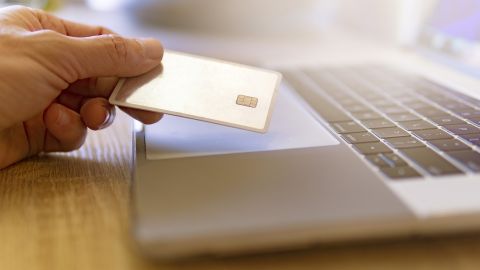 Foto de la mano de una persona sosteniendo una tarjeta frente a una laptop