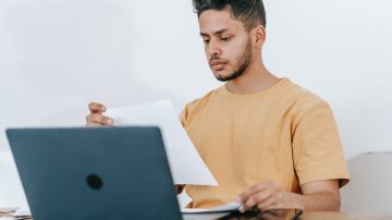 Foto de una persona leyendo papeles frente a una laptop