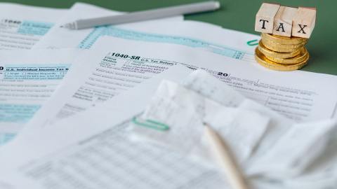 Foto de varios formularios del IRS con algunas monedas al fondo