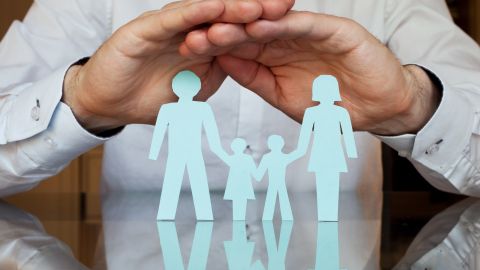 Foto de una persona con las manos sobre una figura de papel que representa una familia