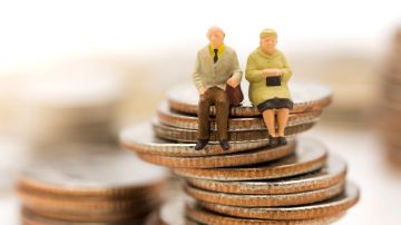 Foto de dos figuras que representan a una pareja de ancianos sentados sobre monedas