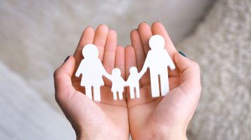 Foto de las manos de una persona sosteniendo una figura de papel que representa a una familia