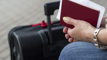 Foto de las manos de una persona sosteniendo una maleta al lado de una maleta.