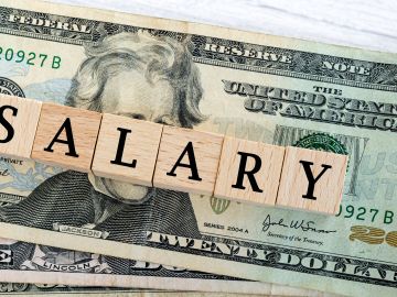 Foto de la palabra "salary" escrita con bloques de madera sobre dólares