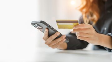 Foto de una mujer sosteniendo su tarjeta de crédito y un teléfono