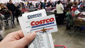 Una mano que sostiene un recibo y una tarjeta de membresía de Costco en el almacén de Costco.