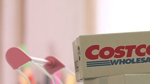 Cajas con el logo de COSTCO WHOLESALE en el carrito de compras cerca de la computadora.