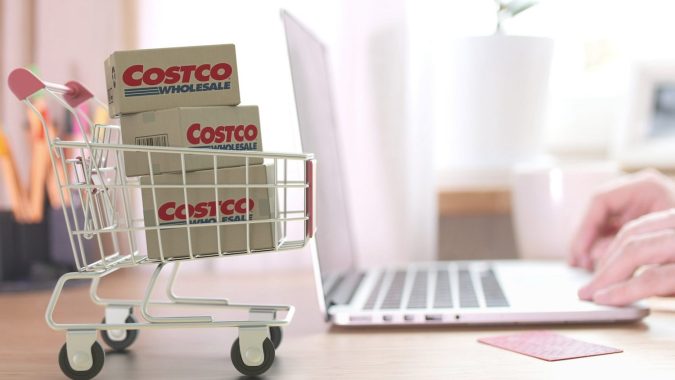 Cajas con el logo de COSTCO WHOLESALE en el carrito de compras cerca de la computadora.