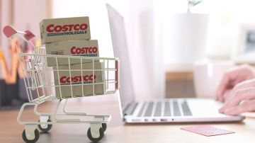 Cajas con el logo de COSTCO WHOLESALE en el carrito de compras cerca de la computadora.