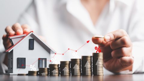 Mano apila monedas con una flecha hacia arriba representando las tasas de interés de una hipoteca.