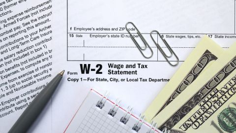 Bolígrafo, libreta y dólares sobre el formulario de impuestos W-2.