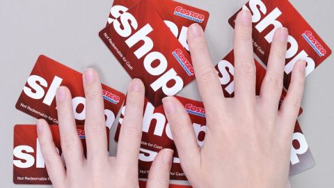 Mano sostiene las tarjetas de regalo de color rojo al por mayor de Costco sobre fondo gris.