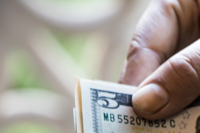 Mano sacando un billete de $5 dólares de una cartera.