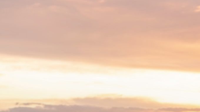 Joven nómada digital sentado en un muelle de madera en el mar trabajando en Internet remotamente al atardecer.