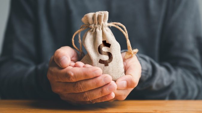 Manos de hombre sostienen una bolsa de dinero que representa un préstamo de emergencia.