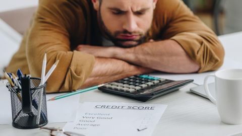 Hombre triste con los ojos cerrados tumbado en la mesa tras ver su puntaje crediticio.