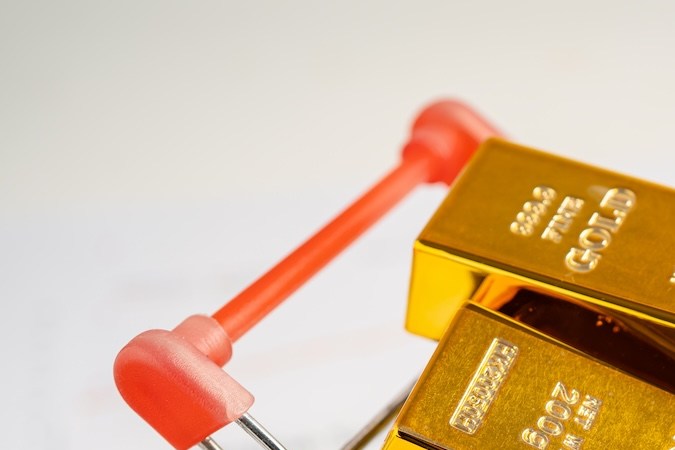 Barra de oro en carrito de compras sobre dólares.