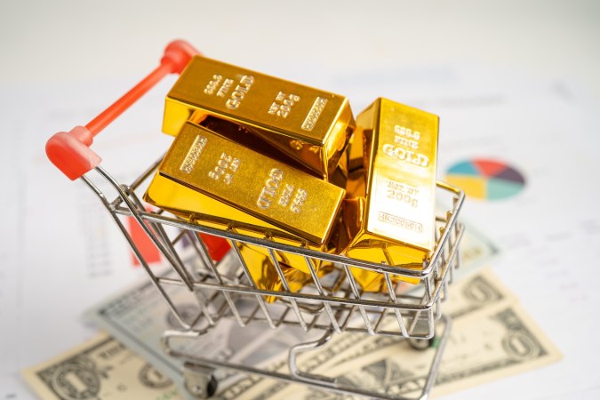 Barra de oro en carrito de compras sobre dólares.