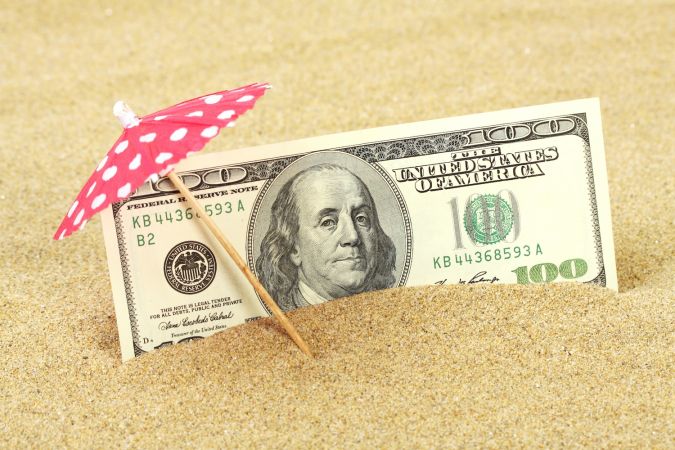 Dinero billetes de cien dólares americanos en la arena de la playa bajo la sombrilla de puntos rojos y blancos.