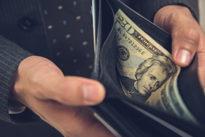 Un hombre abriendo una billetera mostrando algo de dinero, queda un billete de 20 dólares estadounidenses.