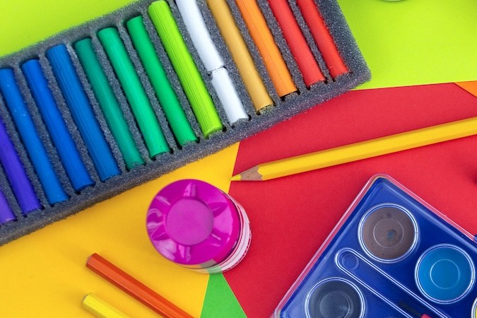 Vista plana desde arriba del lugar de trabajo artístico, acuarelas y tizas pastel en amarillo, naranja, rojo, verde.