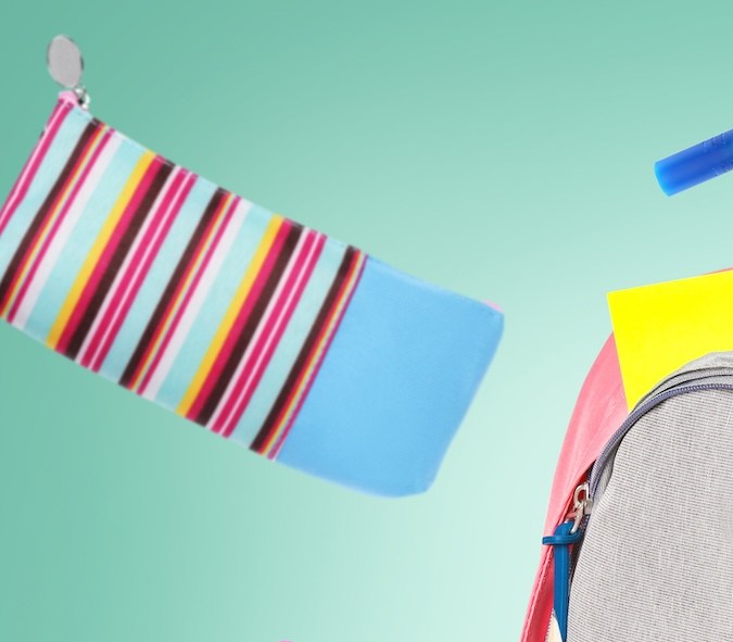 Mochila rodeada de papelería de la escuela de vuelo sobre fondo verde pálido.