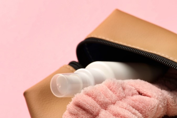 Neceser compacto con diferentes productos cosméticos sobre fondo rosa, primer plano.