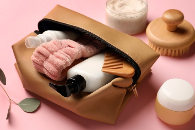 Neceser compacto con diferentes productos cosméticos sobre fondo rosa, primer plano.