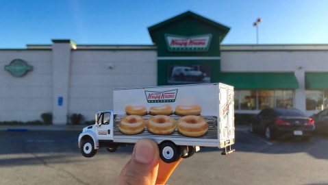 Mano sosteniendo un camión de juguete Krispy Kreme donuts frente a la tienda de donuts Krispy Kreme en California, Estados Unidos.