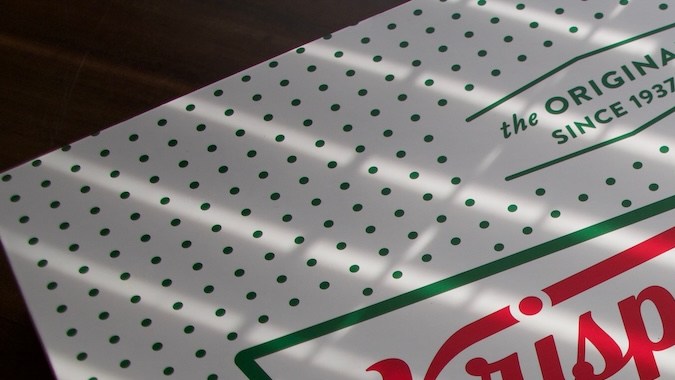 logotipo de Krispy Kreme en una caja de donuts bajo la sombra de la luz solar natural.