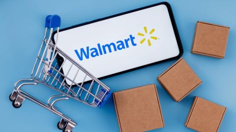Smartphone con logo de Walmart en pantalla, carrito de compras y paquetes.