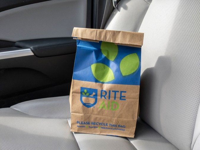 Vista en ángulo de una bolsa de papel marrón Rite Aid sentada dentro de un automóvil, con una receta en el interior.