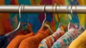 Mujer latina sonriente frente a un estante con ropa colgada.