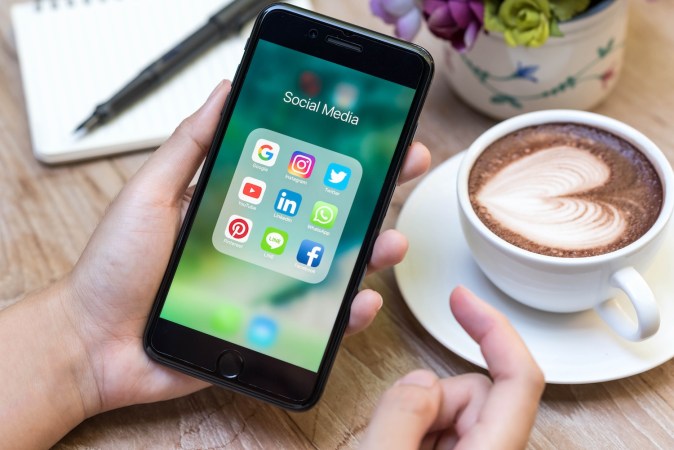 Manos que usan el color negro azabache iPhone7 Plus con íconos de redes sociales en la pantalla.