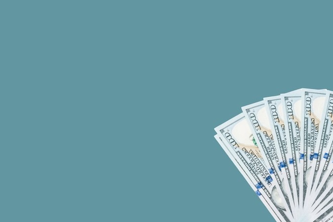 Mano de una estatua femenina en un teléfono móvil que sostiene un fajo de billetes de cien dólares y se los pasa a otra persona sobre un fondo azul verdoso.