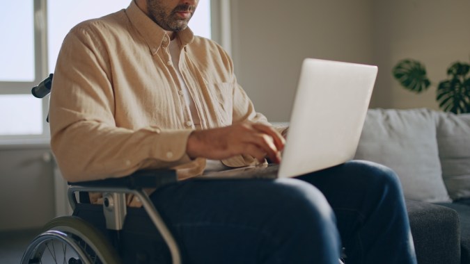Hombre con discapacidad trabajando con una computadora portátil en silla de ruedas, trabajo independiente.