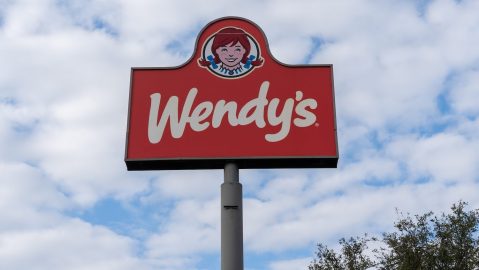 Un cartel en un poste de un restaurante Wendy's con un cielo azul de fondo.