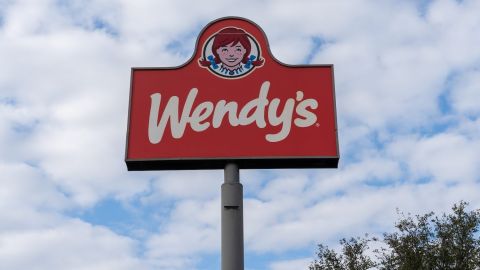 Un cartel en un poste de un restaurante Wendy's con un cielo azul de fondo.